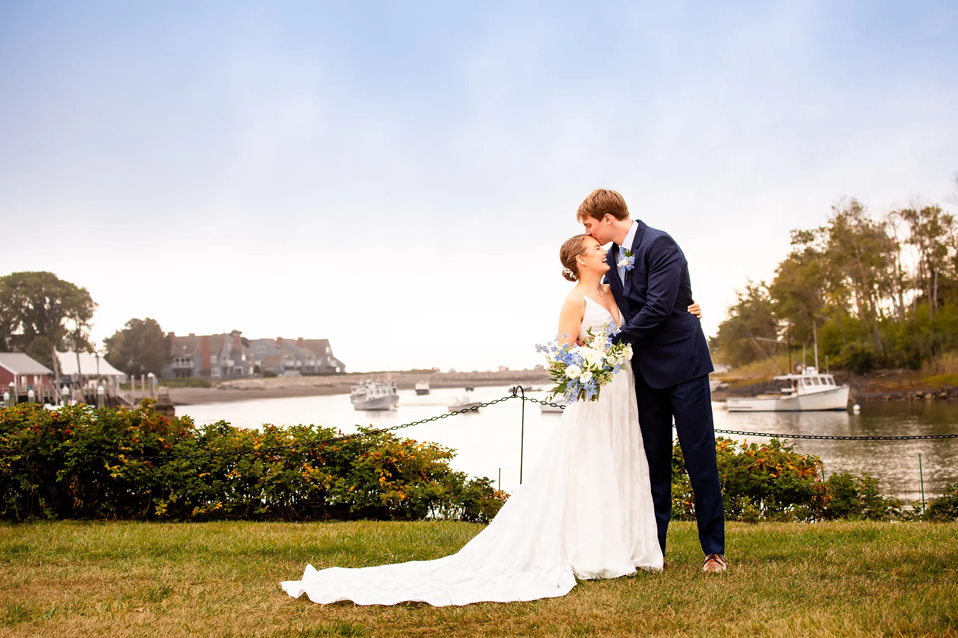 A bride smiles as a groom kisses her on the head during wedding portraits at the Nonantum Resort in Kennebunkport, Maine.