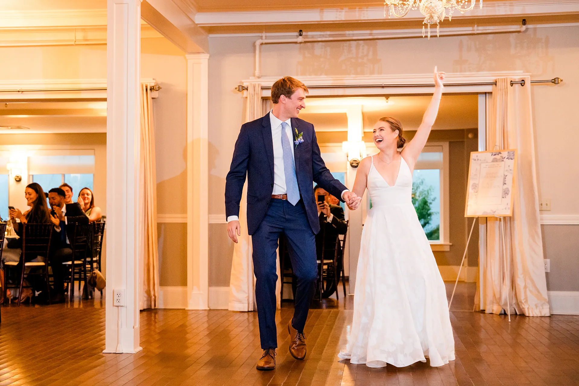 A bride and groom hold hands and laugh as they walk into their wedding reception at the Nonantum Resort in Kennebunkport, Maine.